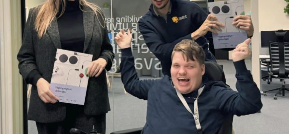 En kvinne og to menn holder jublende opp en skriftlig publikasjon.